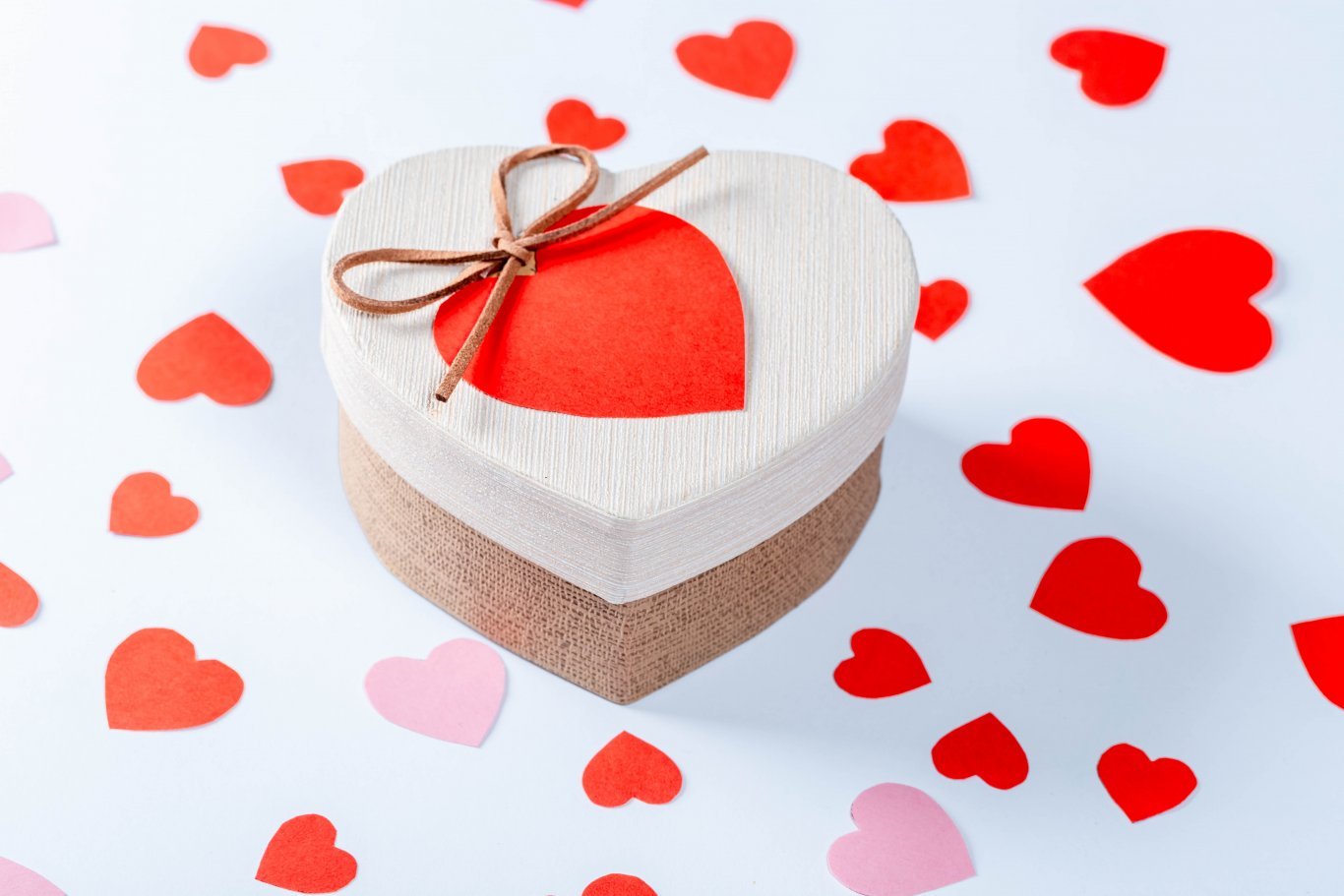 Geschenk zu Valentinstag in Herzform umgeben von vielen Herzen auf weißem Hintergrund